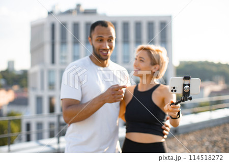 Sporty man and woman writing blog using phone on rooftop. Sporty man and woman writing blog using phone on rooftop. 114518272