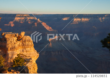 Breathtaking view of Grand Canyon at sunrise or sunset. Intricate layers showcase rugged terrain under warm light. Clear blue sky. Located in Arizona, USA. Breathtaking view of Grand Canyon at sunrise or sunset. Intricate layers showcase rugged terrain under warm light. Clear blue sky. Located in Arizona, USA. 114520651