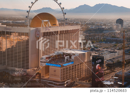Las Vegas Strip view at sunset with a large hotel casino and prominent Ferris wheel in the background. Vibrant scene with mountain silhouettes and golden hour lighting. Las Vegas Strip view at sunset with a large hotel casino and prominent Ferris wheel in the background. Vibrant scene with mountain silhouettes and golden hour lighting. 114520683