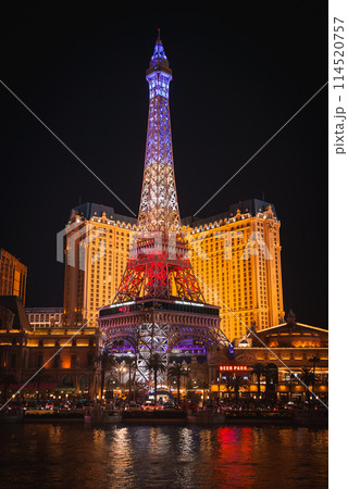 Vibrant night scene on the Las Vegas Strip, showcasing the Eiffel Tower replica at Paris Las Vegas Hotel and Casino. Illuminated in blue, with a bustling atmosphere below. 114520757