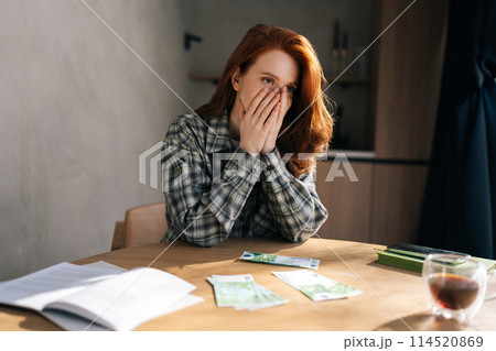 Desperate young woman counting money with sad expression, sitting at home kitchen table. Sad female having financial literacy and loan repayment. Concept of financial crisis. Desperate young woman counting money with sad expression, sitting at home kitchen table. Sad female having financial literacy and loan repayment. Concept of financial crisis. 114520869