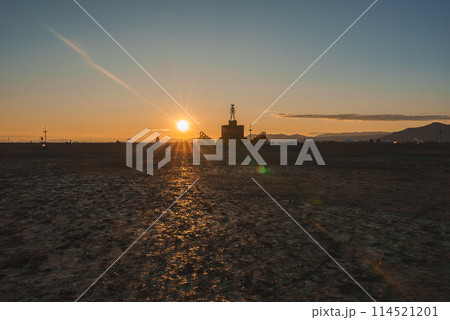 Serene desert landscape at sunset with warm golden glow, silhouetted structure, distant mountains, and festival vibes. Location unspecified, possible remote desert setting. 114521201