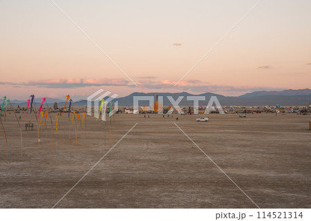 Desert landscape at sunrise or sunset with soft pastel skies, mountain range, colorful art installations, and festival structures in the background. Tranquil atmosphere, location unspecified. Desert landscape at sunrise or sunset with soft pastel skies, mountain range, colorful art installations, and festival structures in the background. Tranquil atmosphere, location unspecified. 114521314