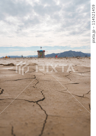 Desert landscape with cracked, dry earth in foreground, colorful tower in the background. Remote location, unique festival vibe. Expansive sky, mountains. Desert landscape with cracked, dry earth in foreground, colorful tower in the background. Remote location, unique festival vibe. Expansive sky, mountains. 114521459