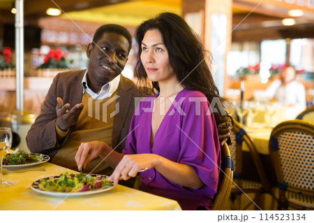 Cheerful african american man flirting with asian woman in restaurant Cheerful african american man flirting with asian woman in restaurant 114523134
