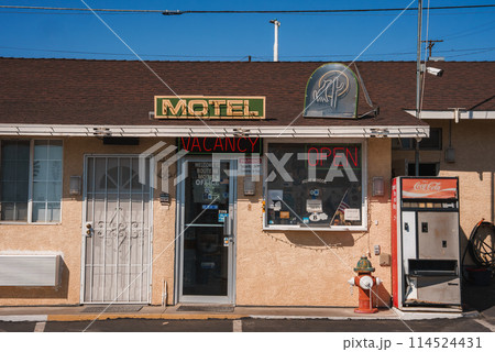 Explore a classic American motel in Barstow on Route 66. Retro neon signs, vintage Coca Cola machine, and nostalgic gas pump create a vintage atmosphere under the sunny desert sky. 114524431