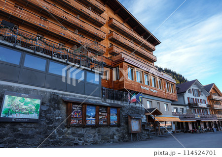 Alpine style building Hotel Eiger with wooden facade, glass windows, and balconies, located in a mountainous region with clear skies. Ideal for outdoor activities. 114524701