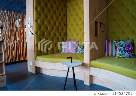 Modern, stylish interior with vibrant chartreuse tufted wall, colorful throw pillows on bed, sleek round table, and unique wooden screen or partition. Dark gray tile floor, ambient lighting. 114524703