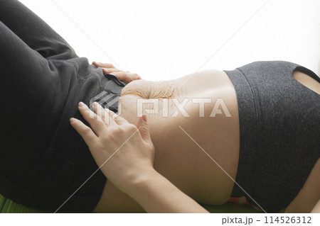 産後の妊娠線が残るお腹とヨガマットの上で仰向けで寝転ぶ女性 産後の妊娠線が残るお腹とヨガマットの上で仰向けで寝転ぶ女性 114526312