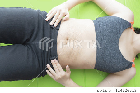 産後の妊娠線が残るお腹とヨガマットの上で仰向けで寝転ぶ女性 114526315