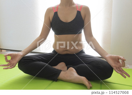 産後の妊娠線が残るお腹とヨガマットの上で胡坐をかき手を合わせ、ヨガの合掌ポーズをする女性 114527008