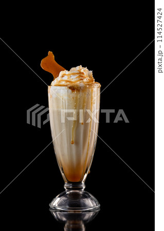Closeup glass of caramel milkshake decorated with syrup and whipped cream isolated at black background. Closeup glass of caramel milkshake decorated with syrup and whipped cream isolated at black background. 114527424