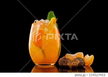 Closeup glass of orange tangerine fresh juice with ice cubes and a group of mandarin slices and figs isolated at black background. 114527453