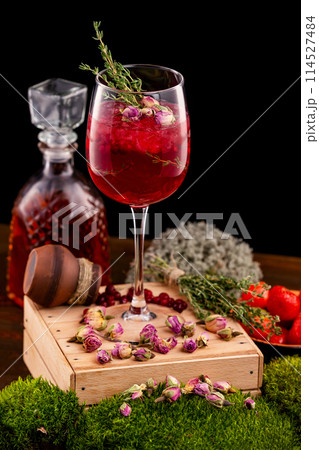 Vertical image of glass with wine alcohol cocktail decorated with cranberry, rosemary and rose flowers at wooden table background. Vertical image of glass with wine alcohol cocktail decorated with cranberry, rosemary and rose flowers at wooden table background. 114527484