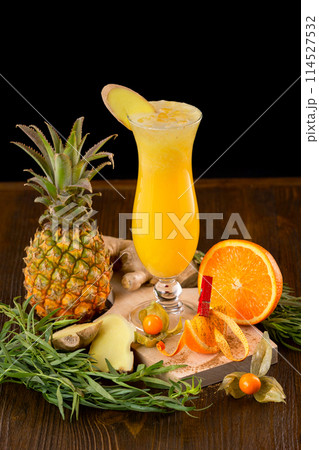 Closeup glass of fresh orange and pineapple juice decorated with ginger and fruits on a wooden table isolated at black background. 114527532