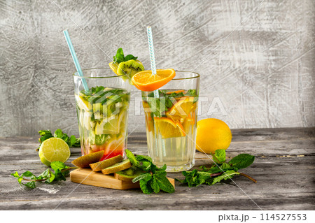 Two glasses of detox water with lemon, kiwi, orange and mint at concrete decorated table background. Concept of healthy lifestyle. 114527553
