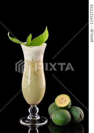 Glass of fresh pineapple guava smootjie decorated with basil isolated at black background. 114527559