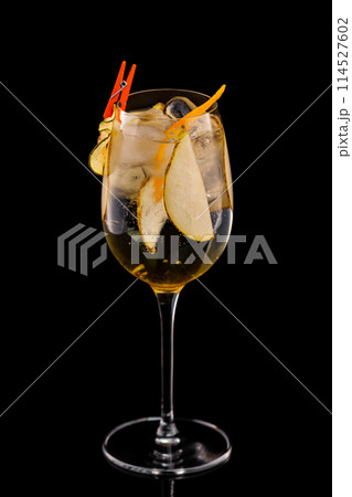 Glass of fizz cocktail with white sparkling wine and pear decorated with lemon chips isolated at black background. 114527602