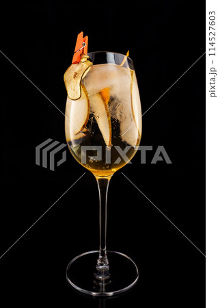 Glass of fizz cocktail with white sparkling wine and pear decorated with lemon chips isolated at black background. Glass of fizz cocktail with white sparkling wine and pear decorated with lemon chips isolated at black background. 114527603