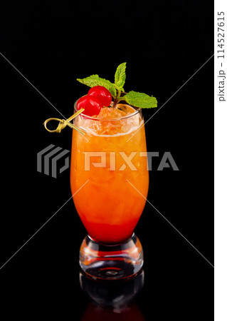 Closeup glass of fresh orange tequila sunrise cocktail decorated with mint and cherry isolated at black background. Closeup glass of fresh orange tequila sunrise cocktail decorated with mint and cherry isolated at black background. 114527615