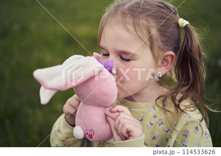 a beautiful blond girl with her toy bunny is playing in the field 114533626