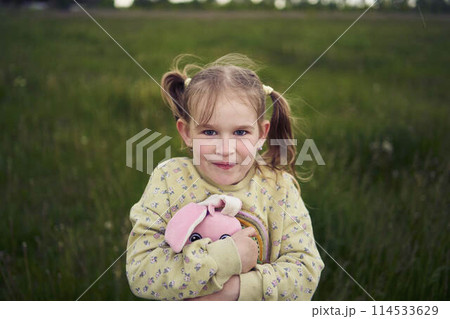 a beautiful blond girl with her toy bunny is playing in the field 114533629