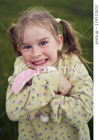 a beautiful blond girl with her toy bunny is playing in the field 114533632