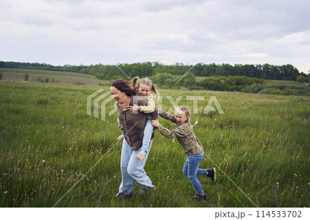 a mother rolls her daughters on her back, playing horse, kisses and hugs a mother rolls her daughters on her back, playing horse, kisses and hugs 114533702