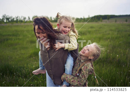 a mother rolls her daughters on her back, playing horse, kisses and hugs 114533825