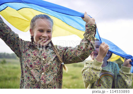 two little girls in the field under the Ukrainian flag in rain 114533893