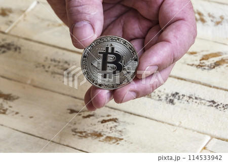 Hand holding a Silver bitcoin coin on a wooden surface background 114533942