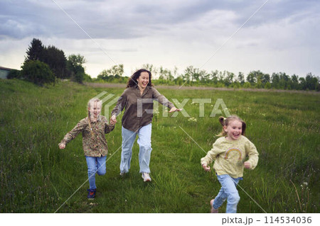 mother and children run holding hands in the field 114534036