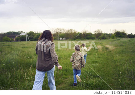 mother and children run holding hands in the field 114534038
