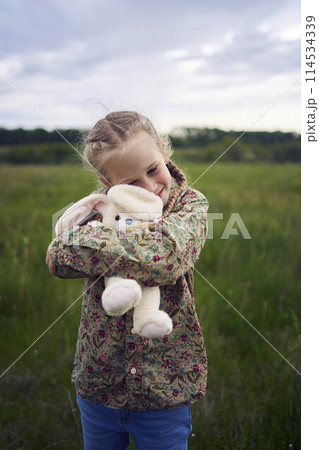 a beautiful blond girl with her toy bunny is playing in the field a beautiful blond girl with her toy bunny is playing in the field 114534339