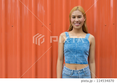 Portrait of beautiful Asian girl with blonde hair against orange background Portrait of beautiful Asian girl with blonde hair against orange background 114534870
