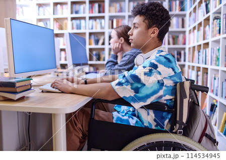 Side view portrait of Middle Eastern teenage boy with disability using computer in school library, copy space Side view portrait of Middle Eastern teenage boy with disability using computer in school library, copy space 114534945
