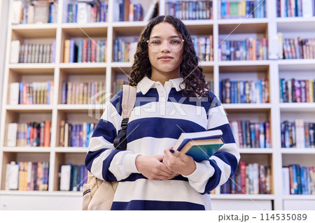 Waist up portrait of young teenage girl wearing glasses standing in school library and holding books with backpack copy space 114535089