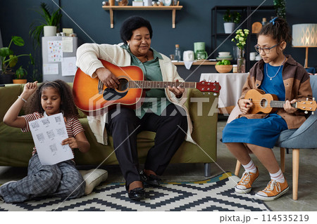 Full length portrait of Black senior woman with two young girls playing musical instruments together indoors 114535219