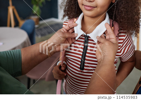 Close up of unrecognizable woman helping daughter getting ready for school in morning and adjusting clothing copy space 114535983