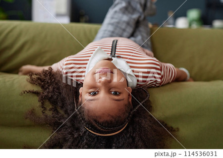 Portrait of young Black girl lying upside down on sofa at home and looking at camera copy space Portrait of young Black girl lying upside down on sofa at home and looking at camera copy space 114536031