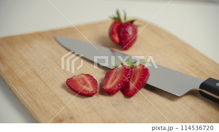 The strawberries are cut into slices. they lie on a wooden board and next to the knife The strawberries are cut into slices. they lie on a wooden board and next to the knife 114536720