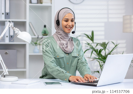 A cheerful professional Muslim woman in a hijab engaged in a customer service call, using a headset and laptop in a modern office. A cheerful professional Muslim woman in a hijab engaged in a customer service call, using a headset and laptop in a modern office. 114537706