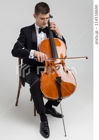 Passionate cello player sitting on chair performing concert Passionate cello player sitting on chair performing concert 114538690