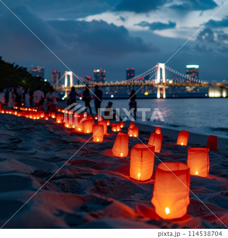 Illuminated paper lanterns line a sandy beach at twilight, with a beautifully lit suspension bridge and city skyline in the background. Japanese Marine Day Umi no Hi also known as Ocean or Sea Days 114538704