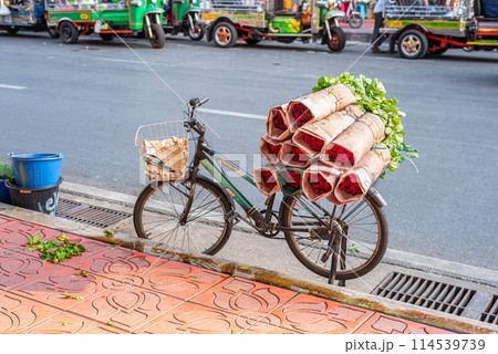 Bicycle loaded with bouquets of roses wrapped in paper with blurred tuk-tuks in the background. Flower market Pak Khlong Talat in Bangkok, Thailand Bicycle loaded with bouquets of roses wrapped in paper with blurred tuk-tuks in the background. Flower market Pak Khlong Talat in Bangkok, Thailand 114539739