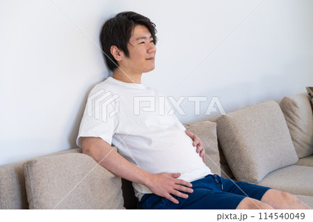 食べ過ぎたお腹をなでる男性 114540049