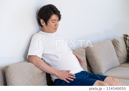食べ過ぎたお腹を見て落ち込む男性 114540050