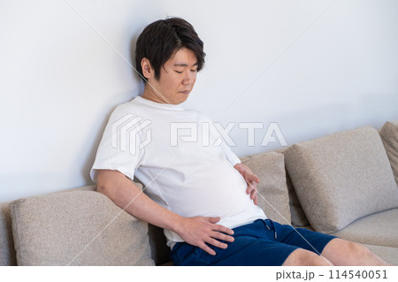 食べ過ぎたお腹を見て落ち込む男性 114540051