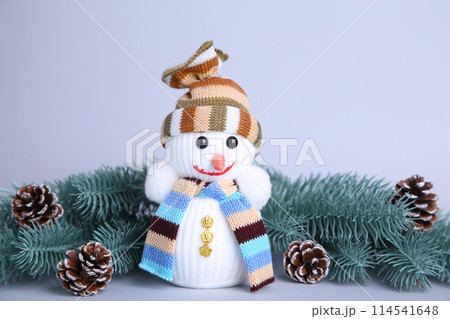 Small snowman toy on a grey background wuth fir-tree branch 114541648