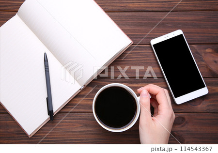 Female hands holding cup of coffee and smartphone on brown wooden background. 114543367